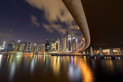 Illuminated buildings by river against sky in city at night