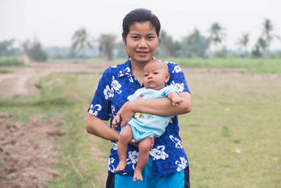 Portrait of woman carrying toddler son while standing on field