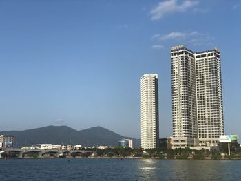 Sea by modern buildings against blue sky