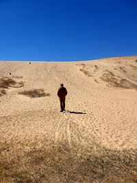 Rear view of man walking on sand in desert against clear blue sky