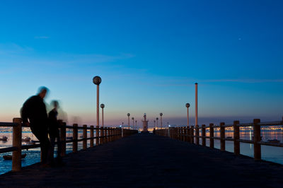 People on pier by sea against blue sky