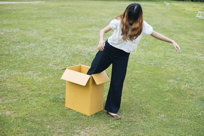 Full length of woman coming out of box on grass