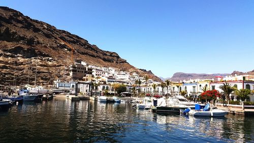 Boats moored at harbor by town against clear sky