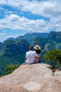 Rear view of woman sitting on mountain against sky