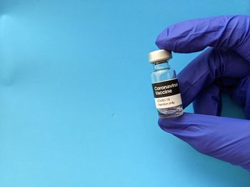 Close-up of hand holding bottle against blue background