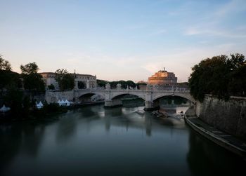 Bridge over river by buildings against sky