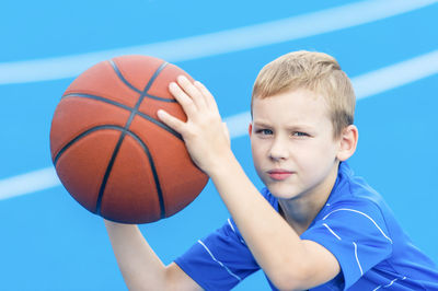 Portrait of boy holding basketball while standing on sports court