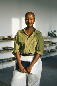 Portrait of confident smiling businesswoman holding document while standing in office