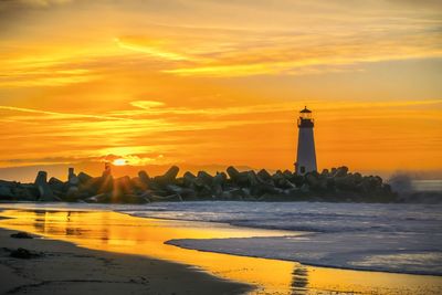 Lighthouse by sea against sky during sunset