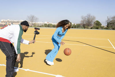 Male filming female friend playing basketball on sports court