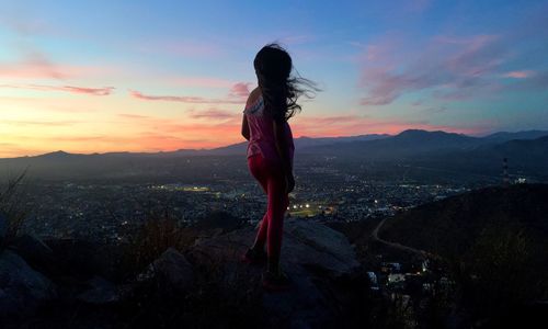 Rear view of woman standing on rock during sunset