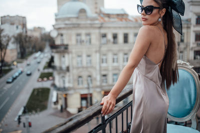 Side view of young woman standing by railing in city