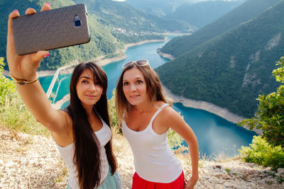 High angle view of female friends taking selfie while standing on cliff against river