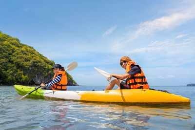 Portrait of people sitting on kayak in sea against sky