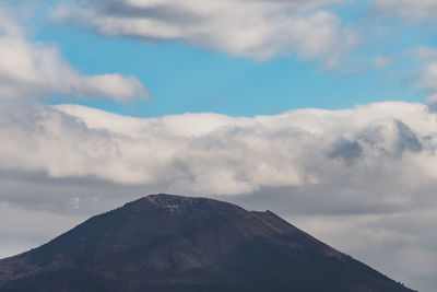 Low angle view of volcanic mountain against cloudy sky