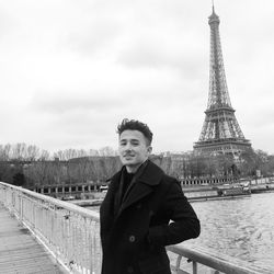 Portrait of smiling man standing by railing with eiffel tower in background against sky