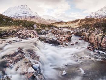 Scenic view of river flowing amidst rocks against sky