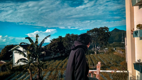 Rear view of man standing by plants against sky