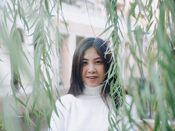 Portrait of smiling young woman standing by plants in park