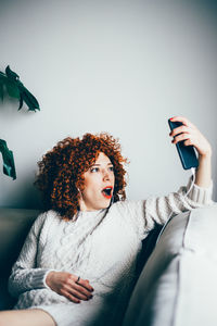 Woman taking selfie while sitting on sofa at home
