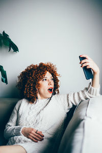 Young woman using mobile phone while sitting on wall