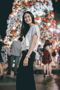 Portrait of smiling young woman standing against tree