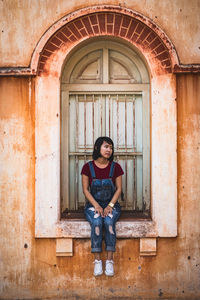 Full length of young woman sitting on window sill in old building