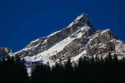 Low angle view of snowcapped mountains against clear blue sky