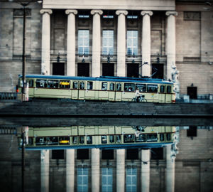 Bus moving on road by building reflecting on calm lake