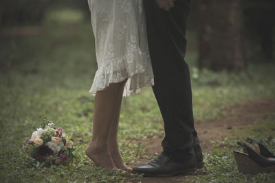 Low section of wedding couple standing on grassy field