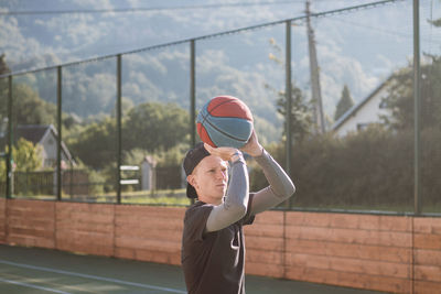 Blond boy in sportswear practices shooting a basketball from behind the three-point line.