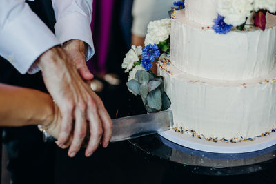 Cropped hands of couple cutting wedding cake