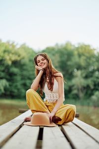 Portrait of young woman sitting on bench against trees