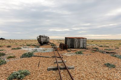 Abandoned boat moored by tracks on field against sky