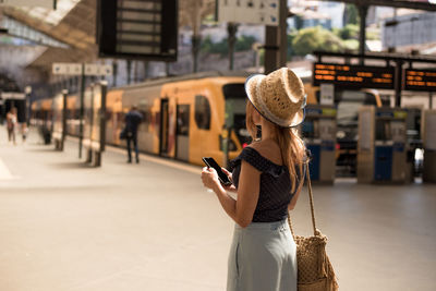 Back view of anonymous female tourist with cellphone on platform against trains in portugal on sunny day