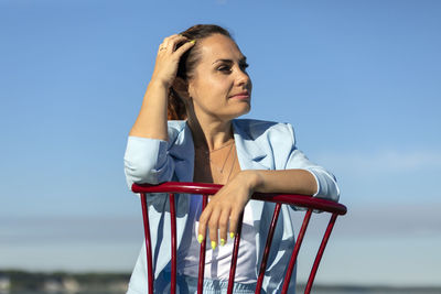 Smiling digital nomad, female business entrepreneur sits in chair in water, blue sky is on