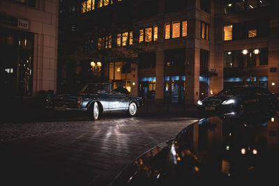 Car on illuminated street amidst buildings at night