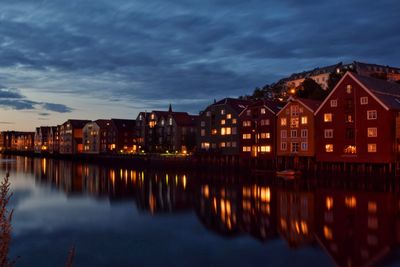 Illuminated buildings by lake against sky at night