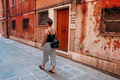 Full length rear view of woman walking on footpath in city