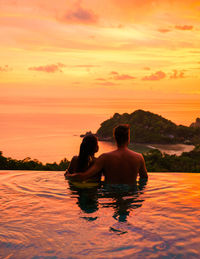 Rear view of man swimming in sea against sky during sunset