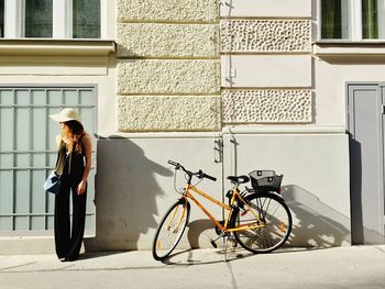 Young woman standing besides bicycle against building