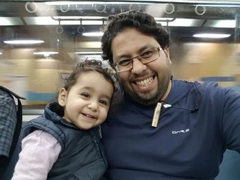 Portrait of cheerful father and daughter sitting at subway station