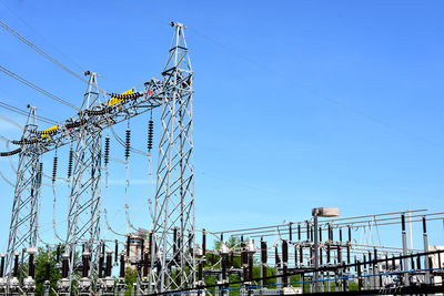 Low angle view of electricity pylon against clear blue sky