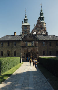 People walking on footpath amidst buildings in copenaghen against sky