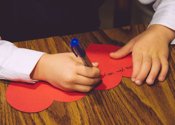 Cropped image of child writing on heart shape greeting card on table