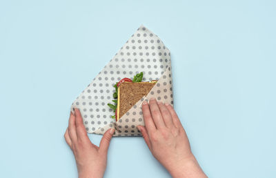 Woman wrapping a sandwich in a beeswax cloth on a blue table, above view. sandwich vegan ingredients