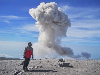 Full length of man standing against smoke erupting against volcanic landscape
