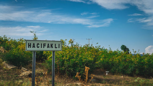 Road sign by trees against sky