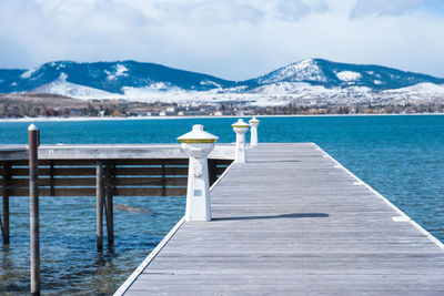 Pier on sea by snowcapped mountains against sky