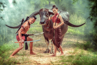 Full length portrait of warriors standing with buffalo in forest